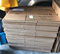 Stack of about 50 flattened cardboard moving boxes with printed graphics and some labeling, showing thickness and texture of corrugated cardboard.