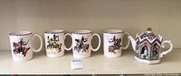 Four large Palissy England mugs with colorful historical English knight illustrations and silver rims, along with one small Sadler hexagonal ceramic teapot decorated with historical figures and geometric patterns.