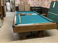 Angled view of pool table showing wood frame, green felt, balls in tray and cues laid across the playing surface