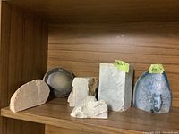 Image showing six rocks aligned on a wooden shelf, a mix of raw and polished stones including geodes and blocks.