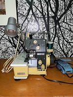 Side view of the vintage Mammylock ML-4 serger sewing machine showing threading, foot pedal, and attached desk lamp