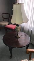 Lamp with hand-painted ceramic base and cream fabric scalloped lampshade placed on round mahogany side table
