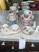 Photo showing an arrangement of multiple vintage teacups and saucers alongside Old Royal creamer and sugar set, Minton dishes, and salt and pepper shakers on a table.