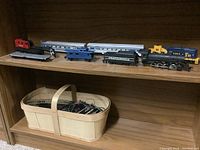 Wide view of the train cars on wooden shelf with basket of tracks holding trains and transformer.