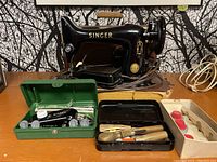 Full view of Singer 99K sewing machine with multiple accessories including green Singer kit, black tool case with scissors and screwdrivers, and additional red and white sewing parts tray.
