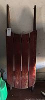 Front view of vintage wooden sled showing red painted slats and metal runners underneath.