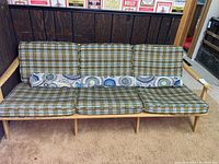 Front view of three-seat wooden sofa with plaid cushions and partial bolt of fabric on seat