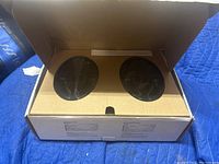 Open box showing two black coaxial speakers inside with protective cardboard.