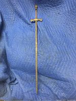 Full view of the sword showing the full length of the steel blade with brass hilt and pommel against a blue quilted background.