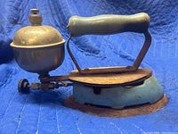 Side angle of vintage Coleman antique gas iron showing blue base, fuel tank, and handle.