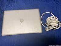 Top view of silver Apple MacBook with visible scratches and white charger cable coiled beside it.