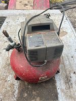 Photo of red portable air compressor with black motor housing and power cord laying on top, showing wear and dirt.