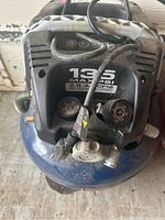 Top view of an air compressor with pressure gauges, power cord, and control panel visible.