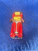 Top view of red 1938 Mercedes-Benz 500K diecast model car on a blue textured surface, showing open doors and detailed yellow interior