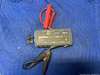 Photo of a Genius Boost HD GB70 2000 amp 12 volt jump starter showing the device and red and black jumper cable clamps.
