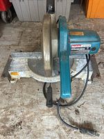 Makita LS1010 miter saw showing top-down view of blade, handle, miter adjustment base, power cord, and some wear from use.