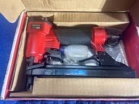 New Arrow PT50 pneumatic stapler in original box, shows stapler from side with padded black grip and red metal upper.