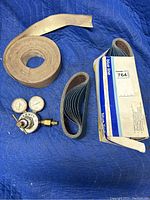 Photo showing the Harris gas gauge with two dials alongside the Blue Line sanding belts stacked and the large roll of 120 grit sandpaper.