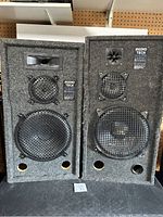 Pair of Audio Tech Pro Poly Series speakers showing full front side with protective metal grills and grey carpet covering.