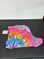 Colorful folded tie-dye beach towel with bright hues of pink, yellow, blue, orange, and purple.