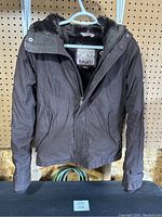 Front view of the brown jacket with visible zipper, pockets, and fur-lined collar.