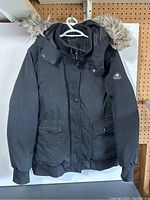 Front view of black women's Canadian jacket with fur-trimmed hood showing buttons, zipper, pockets, and ribbed cuffs.