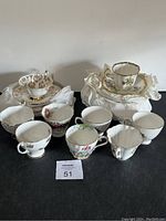 Overview photo showing 8 assorted porcelain tea cups and 8 matching saucers with various floral patterns and gold trim.