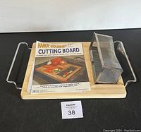 Front view of Handy Gourmet cutting board with metal handles, stainless steel mesh basket, and product information paper on board showing its drain and catch function.