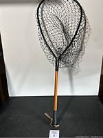 Full view of fishing net with black mesh and orange handle with rope.