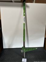 Full view of green garden weeder with handle and digging blade against a white background.