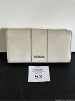 Front view of beige Guess wallet showing embossed 'G' pattern and metal Guess logo plate