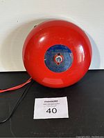 Front view of red steel motorized bell with central blue label showing Mircom branding and model info.