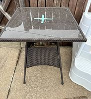Top-down view of square outdoor table with glass top showing surface condition and taped markings.
