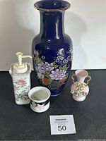Photo showing all four ceramic pieces including the large cobalt blue vase, white pump dispenser, small white container, and pink floral vase.