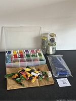 Photo showing organized plastic box with embroidery floss, jars with needles and pins, loose skeins, and fabric bag.