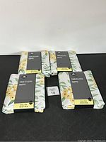 Four Hometrends tablecloths with floral pattern, folded with packaging showing product name and size 52 x 70 inches.