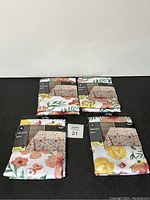Four tablecloths packaged, showing floral patterns and HomeTrends brand.