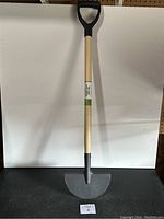 Full view of the turf edger showing the D-shaped black plastic handle, wooden shaft, and curved metal blade.