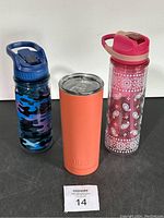 Three water bottles shown side by side on dark surface: blue camo, orange Built tumbler, pink paisley patterned bottle