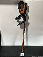 Full view of WORX WG261 cordless hedge trimmer with 22-inch blade showing orange and black design, safety guard, and handle.