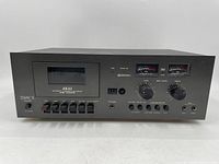 Front view of AKAI CS-705D cassette deck showing cassette compartment, meters, control switches, and inputs.