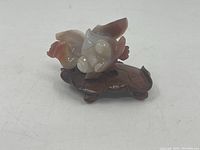 Another front angle photo of the carved stone fish figurine on wooden leaf-shaped stand, highlighting colors and details.