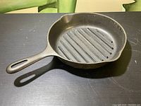 Another angle of the vintage cast iron grill fry pan on black surface highlighting ridged cooking surface and handle.