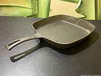 Angled side view of the cast iron square pan showing the handle and inner cooking surface with wear.