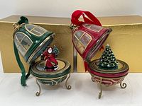 Close-up angle of both Christmas ornaments revealing the detailed gold trim accents, windowed bell shape, and fabric ribbons for hanging.