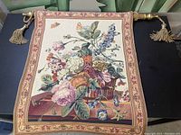 Identical view of the woven floral tapestry with hanging rod and tassels.