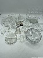 Full view of the large lot of glassware showing serving dishes, plates, bowls, glasses, and shakers arranged on a white surface