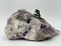 Overall view of the amethyst and quartz mineral specimen with pyrite deposits and a miniature pirate figurine placed on top, showing the rough matrix and crystal formations.