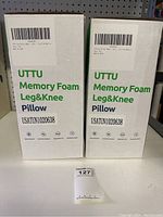 Two white UTTU Memory Foam Leg & Knee Pillow boxes with green and black text, showing front with product name and barcode.