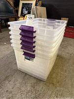 Stack of six clear plastic totes with purple handles, showing dust and dirt on surfaces.